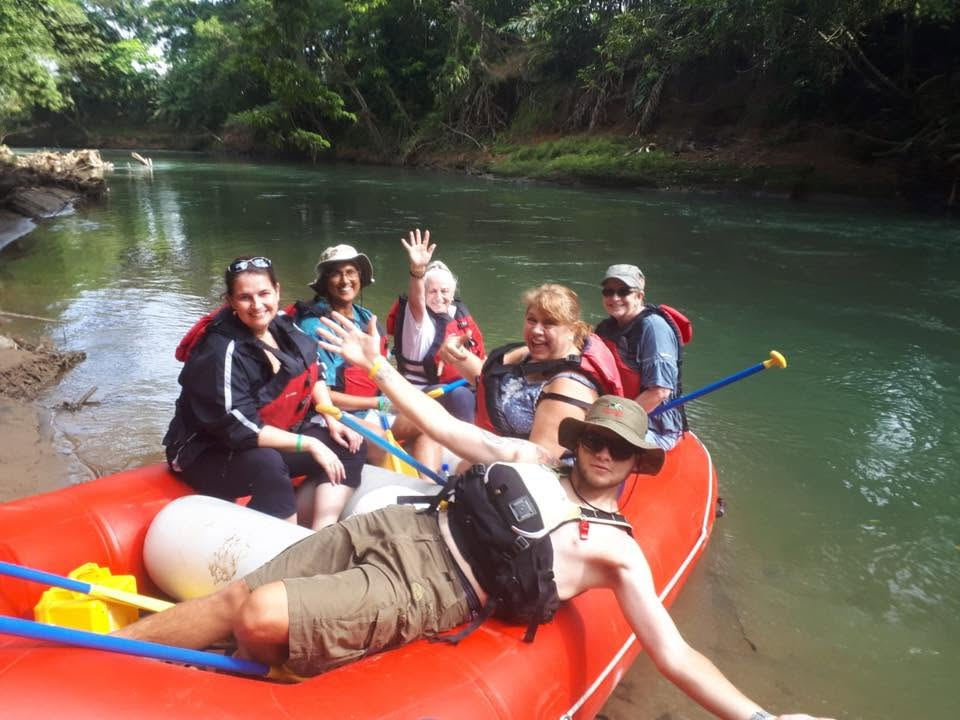 Retreat group smiling and waving from a red raft on a jungle river